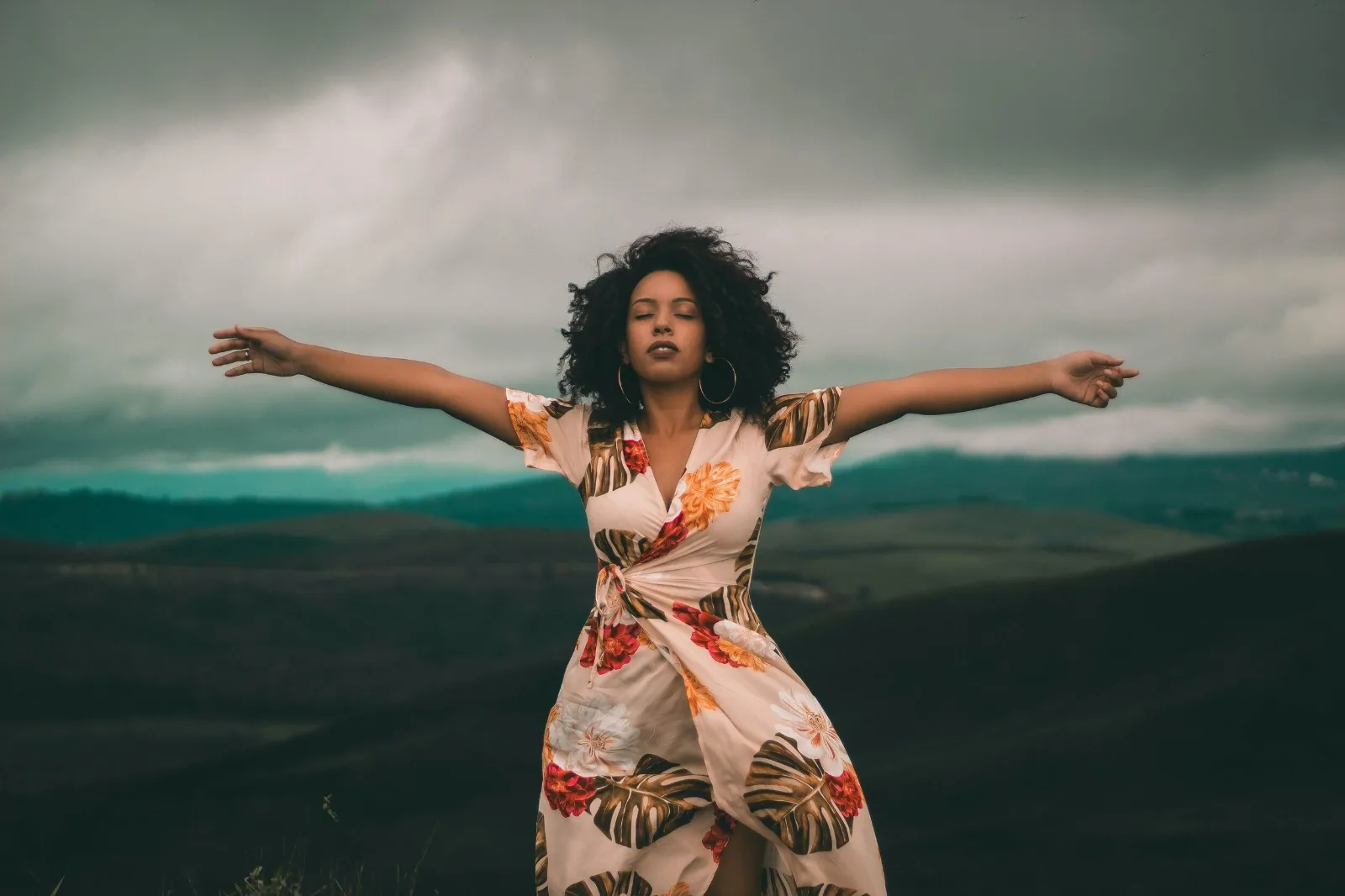 A woman standing outdoors with open arms in a posture of restoration