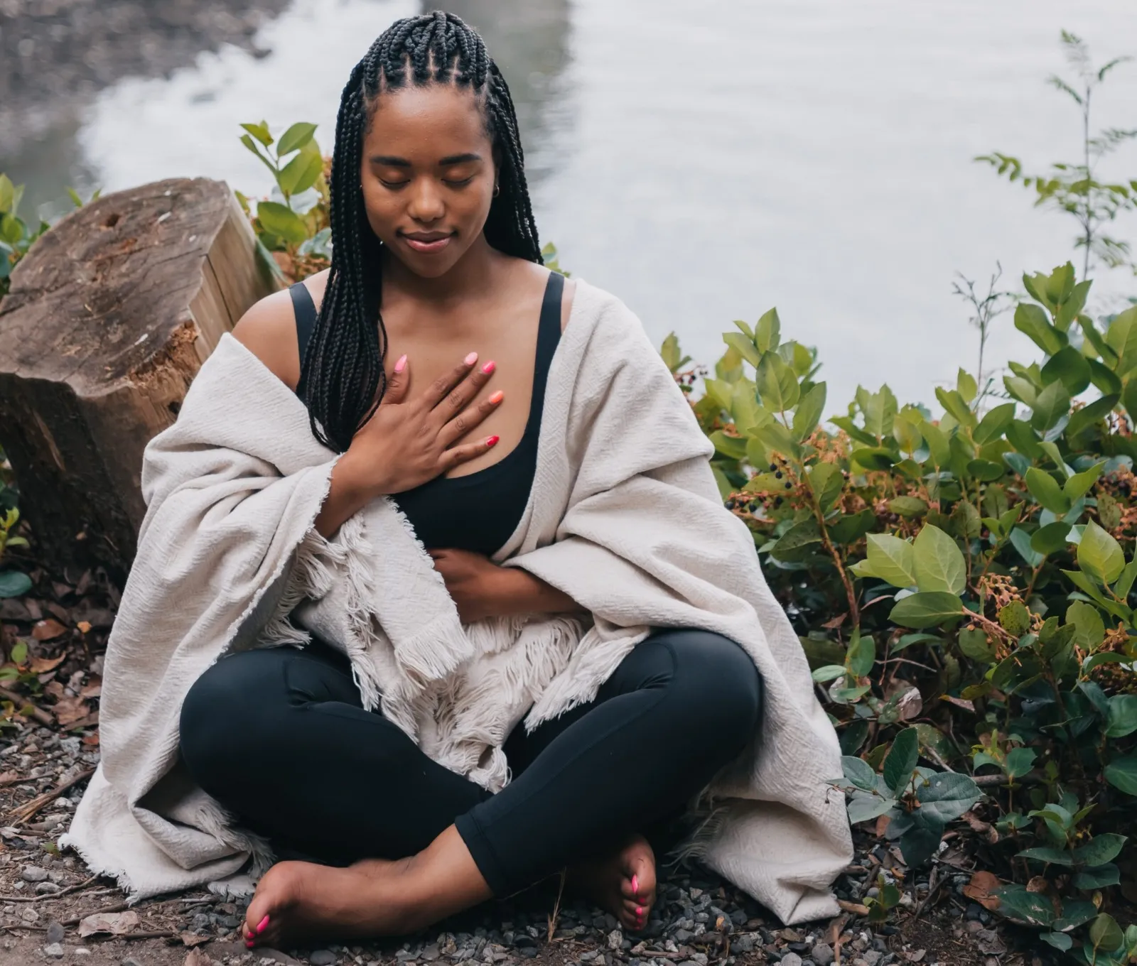 A woman seated beside calm water with her hand over her heart